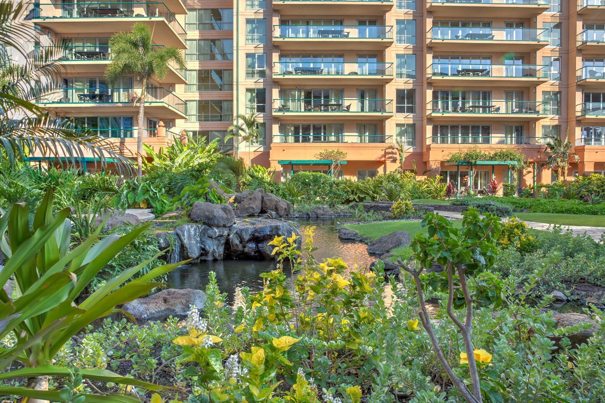 A hotel with multiple balconies, a small pond, and lush greenery.