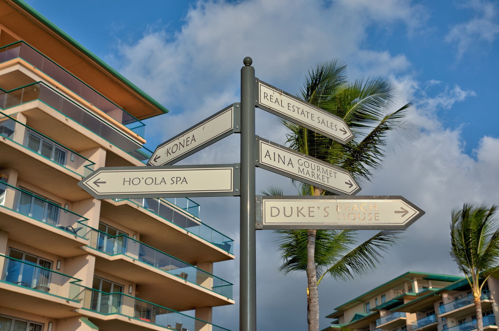 A signpost with directions to various locations including 'Real Estate Sales', 'Aina Gouri Market', 'Ho'ola Spa', and 'Duke's Beach House'.