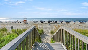 A wooden staircase leading to a beach with umbrellas and lounge chairs. - Charming 15th Floor Condo, Indoor and Outdoor Pool | Crescent Shores - S 1508 (North Myrtle Beach)