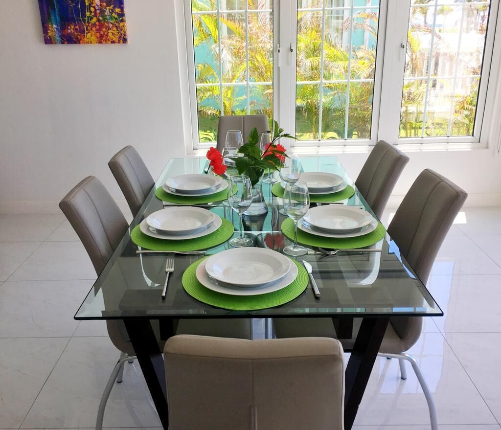 A dining table set for six with green placemats, white plates, and clear glassware.