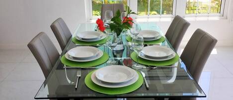 A dining table set for six with green placemats, white plates, and clear glassware.