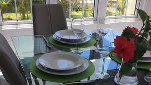 Een eettafel gedekt met borden, glazen en bestek, met uitzicht op groen door grote ramen.