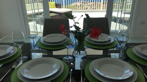 Een eettafel voor zes personen, met groene placemats, witte borden en helder glaswerk. Een vaas met rode bloemen staat in het midden van de tafel.