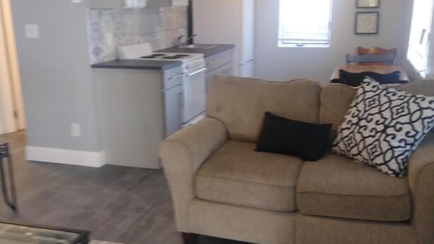Una sala de estar con un sofá color beige, una mesa de centro de cristal y un tapete estampado.