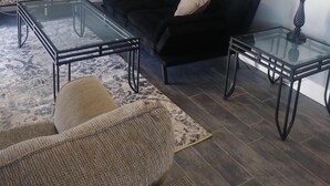 Un salón con un sofá negro, dos mesas de centro de cristal, un globo terráqueo, un cuadro enmarcado y una lámpara.