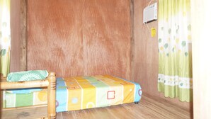 A small, single-bed room with a wooden headboard, a colorful bedspread, and a green curtain.