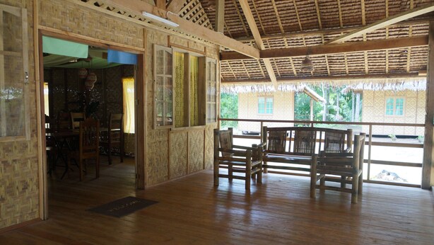 A wooden-floored room with a thatched roof, wooden furniture, and large windows.