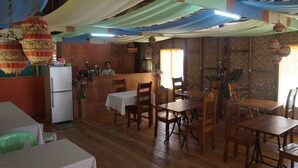 A restaurant with wooden tables and chairs, a refrigerator, and hanging decorations.