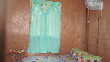 A small room with a bed, a table, a fan, and a curtain.