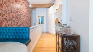 A hallway with a blue cushioned bench, a wooden table with wine glasses, and a floral wallpapered wall. - The Designer's Residence (Auckland)