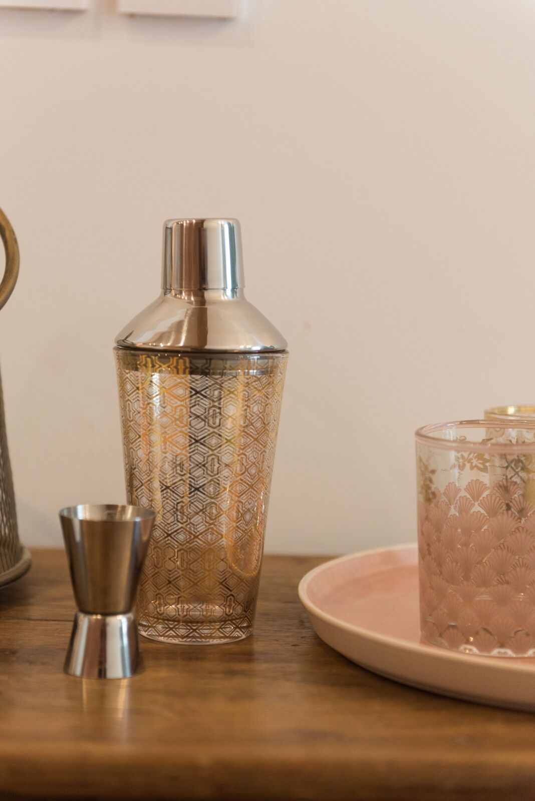 Un shaker à cocktails, un verre et une assiette sur une surface en bois.