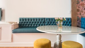 A teal upholstered sofa, a glass table with a vase of flowers, and two mustard-colored ottomans. - The Designer's Residence (Auckland)