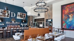 A modern restaurant with wooden tables and booths, a bar area with shelves of bottles, and a large colorful painting on the wall. - Residence Inn Stamford Downtown (Stamford)