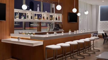 A modern bar area with a long counter, multiple stools, and a variety of bottles and glasses.