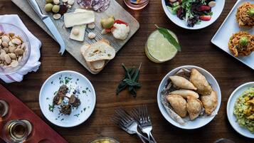 Una variedad de platos, entre ellos una tabla de embutidos, una ensalada y empanadas, acompañados de vasos con bebidas.