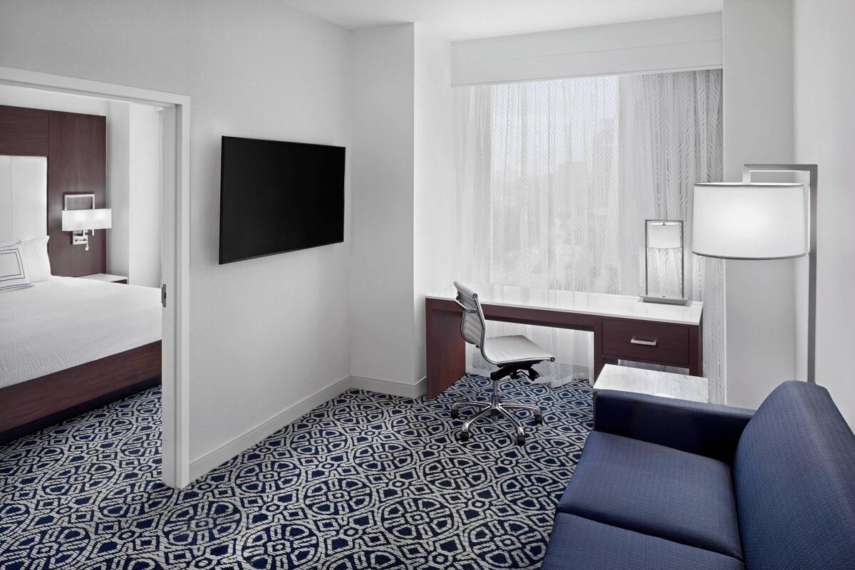 A hotel room with a bed, a desk, a chair, a TV, and a large window with curtains.