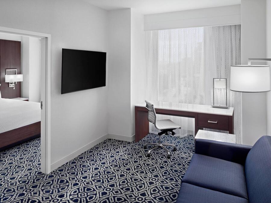 A hotel room with a bed, a desk, a chair, a TV, and a large window with curtains.