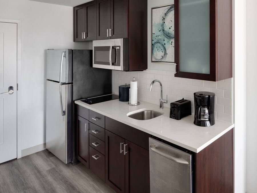 A modern kitchen with dark wooden cabinets, stainless steel appliances, a white countertop, and a dishwasher.