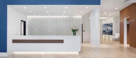 A modern reception area with a white reception desk, a blue accent wall, and a wooden floor.