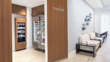 A modern hotel lobby with a wooden reception desk, a seating area with sofas, and a refrigerator stocked with beverages.