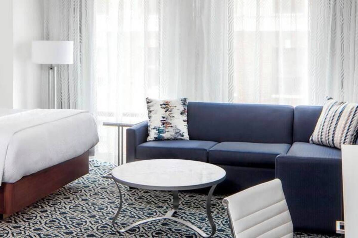 A hotel room with a bed, a sofa, a small table, and a TV.