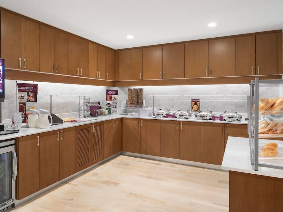 Une cuisine moderne avec des meubles en bois, un réfrigérateur, une machine à café et un présentoir rempli de pâtisseries.