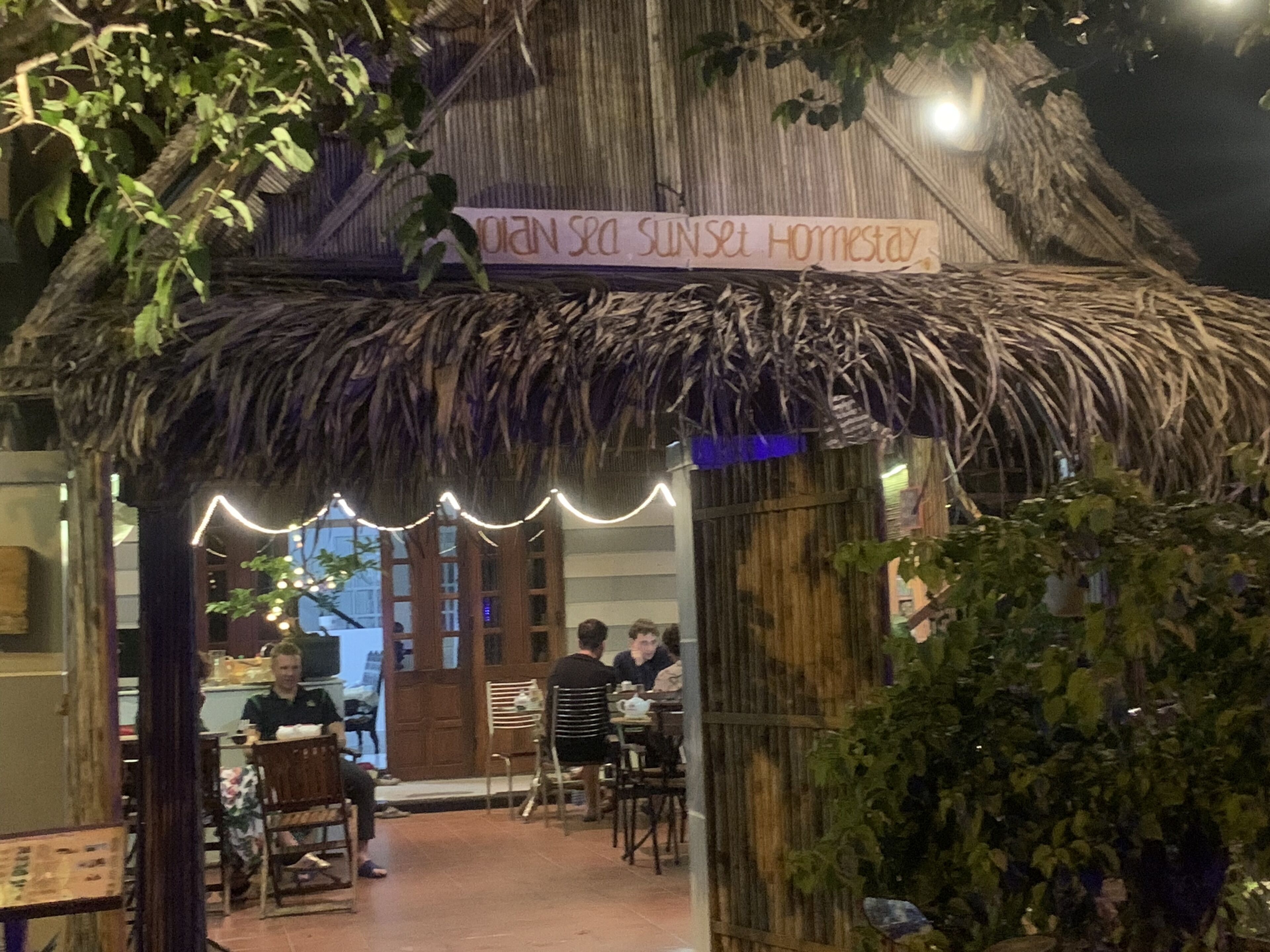 Restaurante con techo de paja e iluminación colgante, con un letrero que dice "DIAN SEA SUNSET HOMESTAY".
