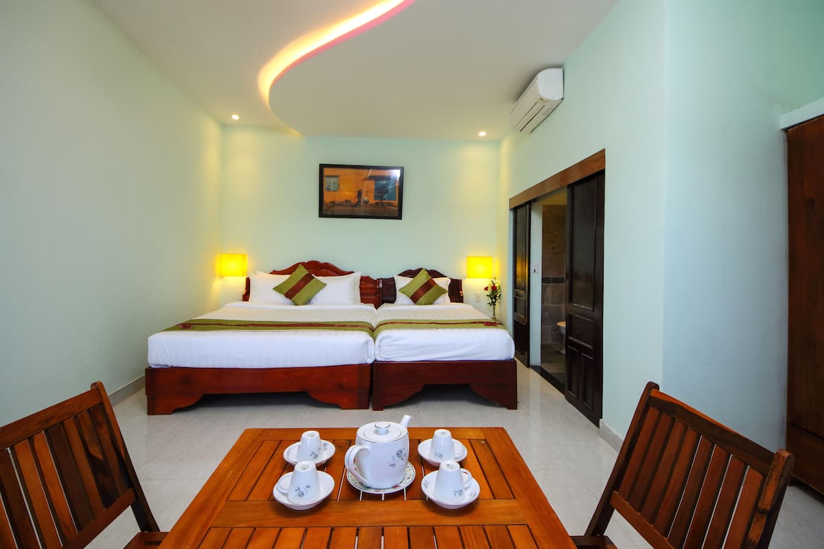 A hotel room with two beds, a table with tea sets, and a painting on the wall.