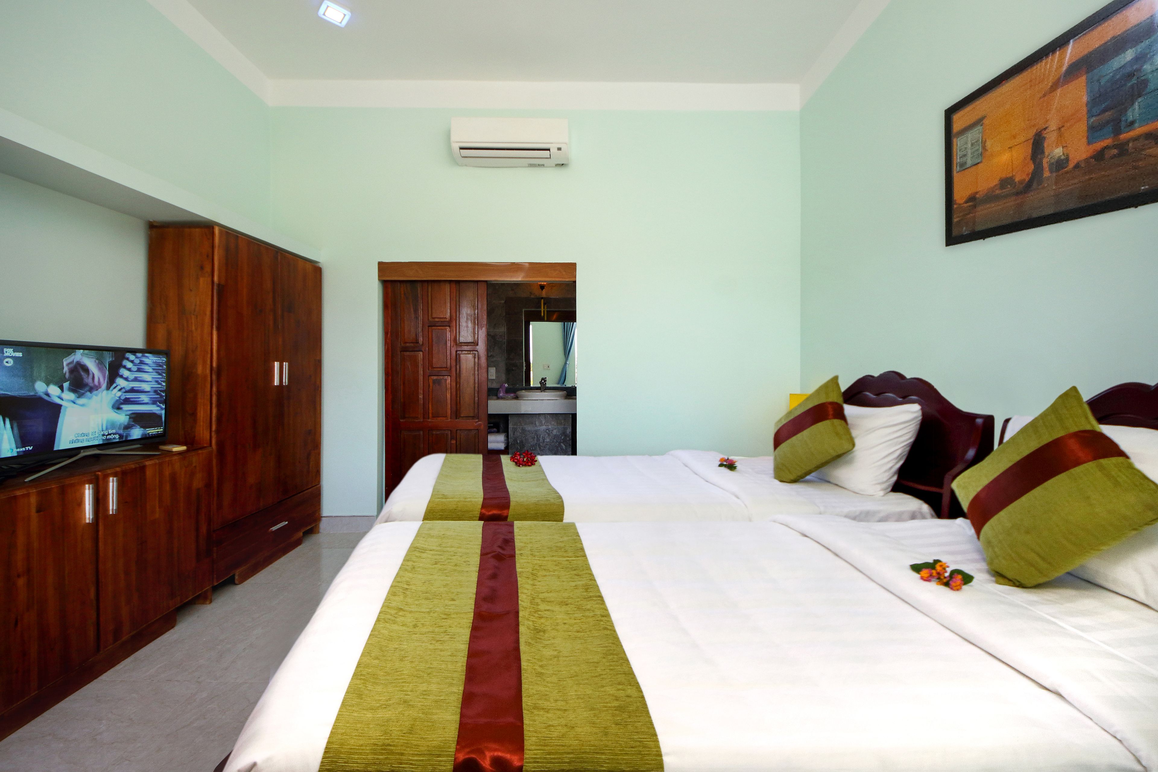 A hotel room with two beds, a wooden wardrobe, a television, and a painting on the wall.