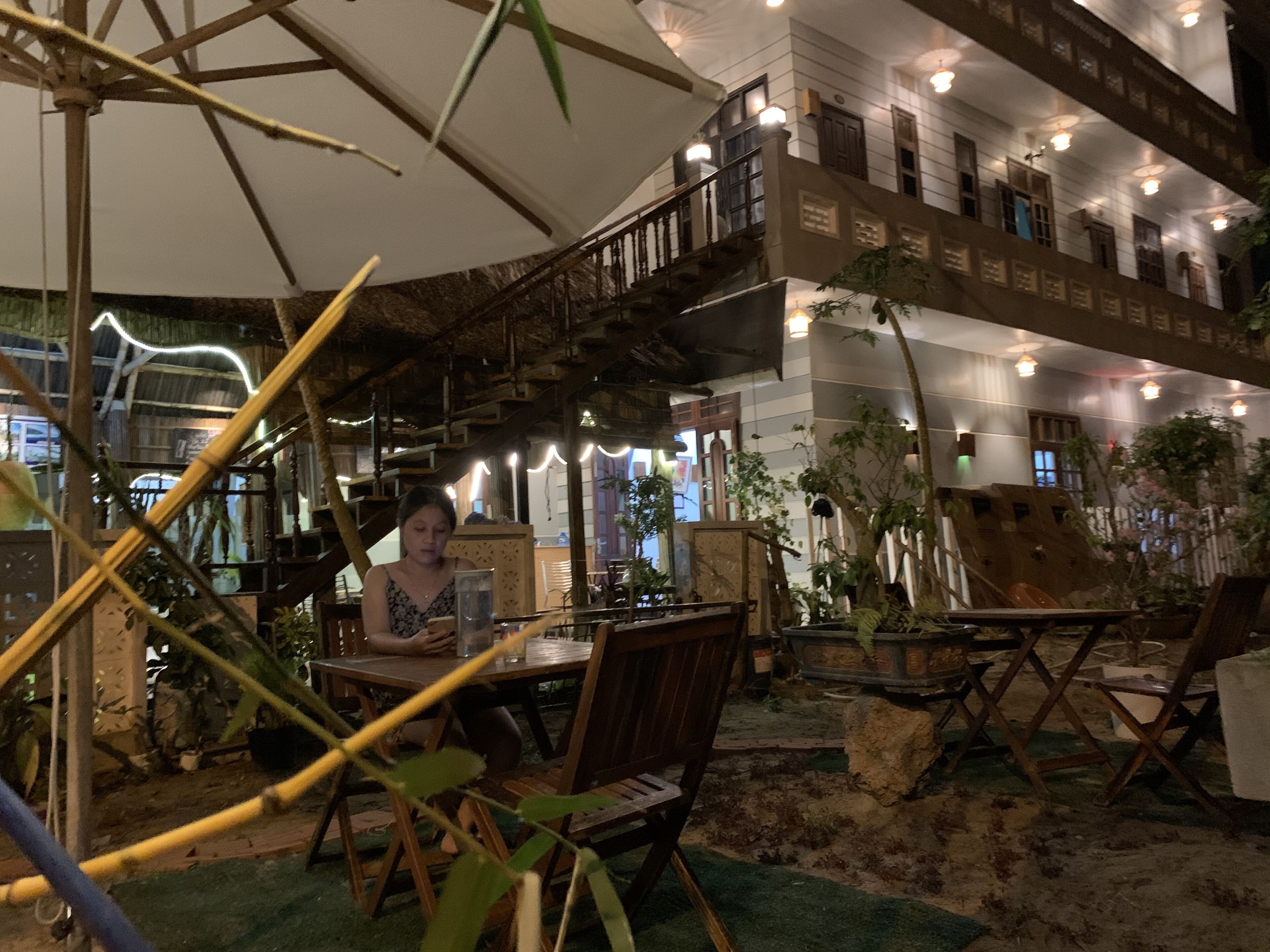 An indoor dining area with a high ceiling, wooden railings, and potted plants.