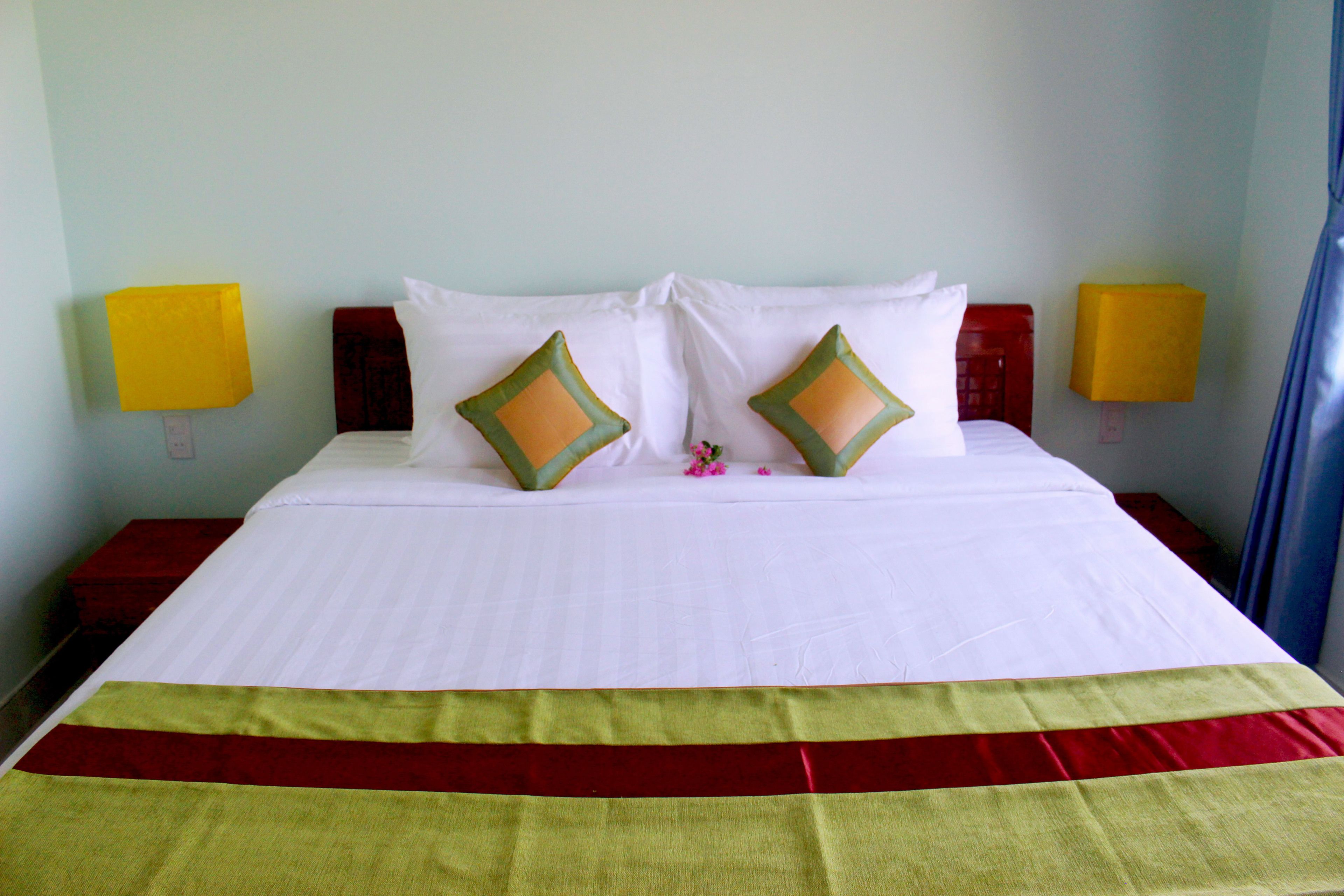 A hotel room with a neatly made bed, two bedside lamps, and a red and yellow striped bedspread.
