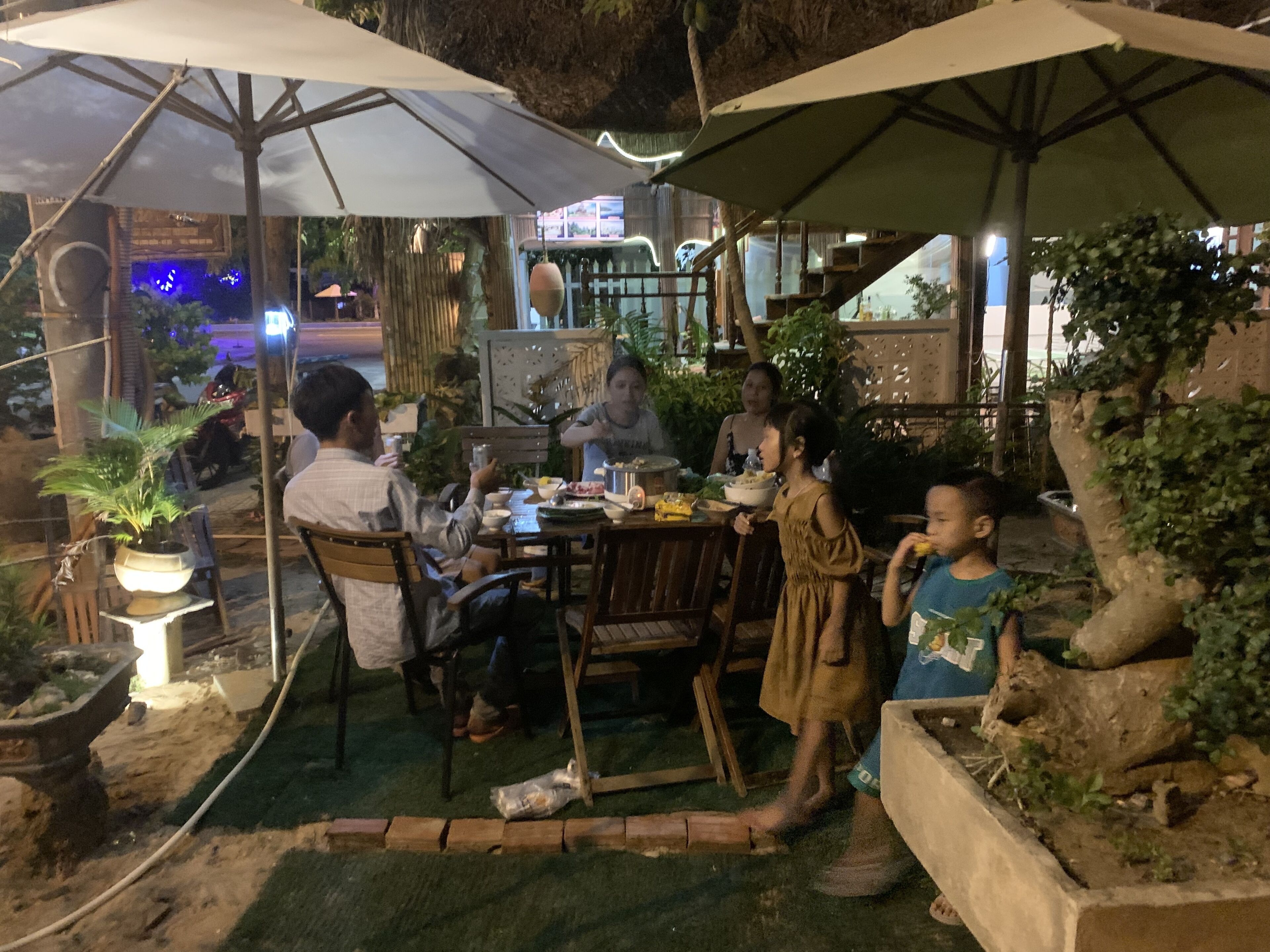 An outdoor dining area with tables and chairs, surrounded by potted plants and umbrellas.