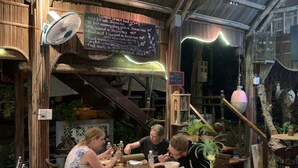 A rustic outdoor dining area with wooden tables and chairs, a chalkboard menu, and a large green vase on the table. - Hoi An Sea Sunset Villa & Bar (Da Nang)