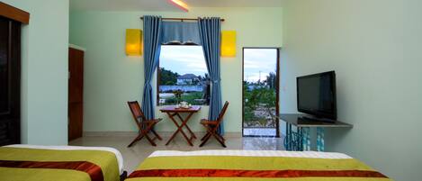 A hotel room with two beds, a TV, a dining table with chairs, and a view of the outdoors.