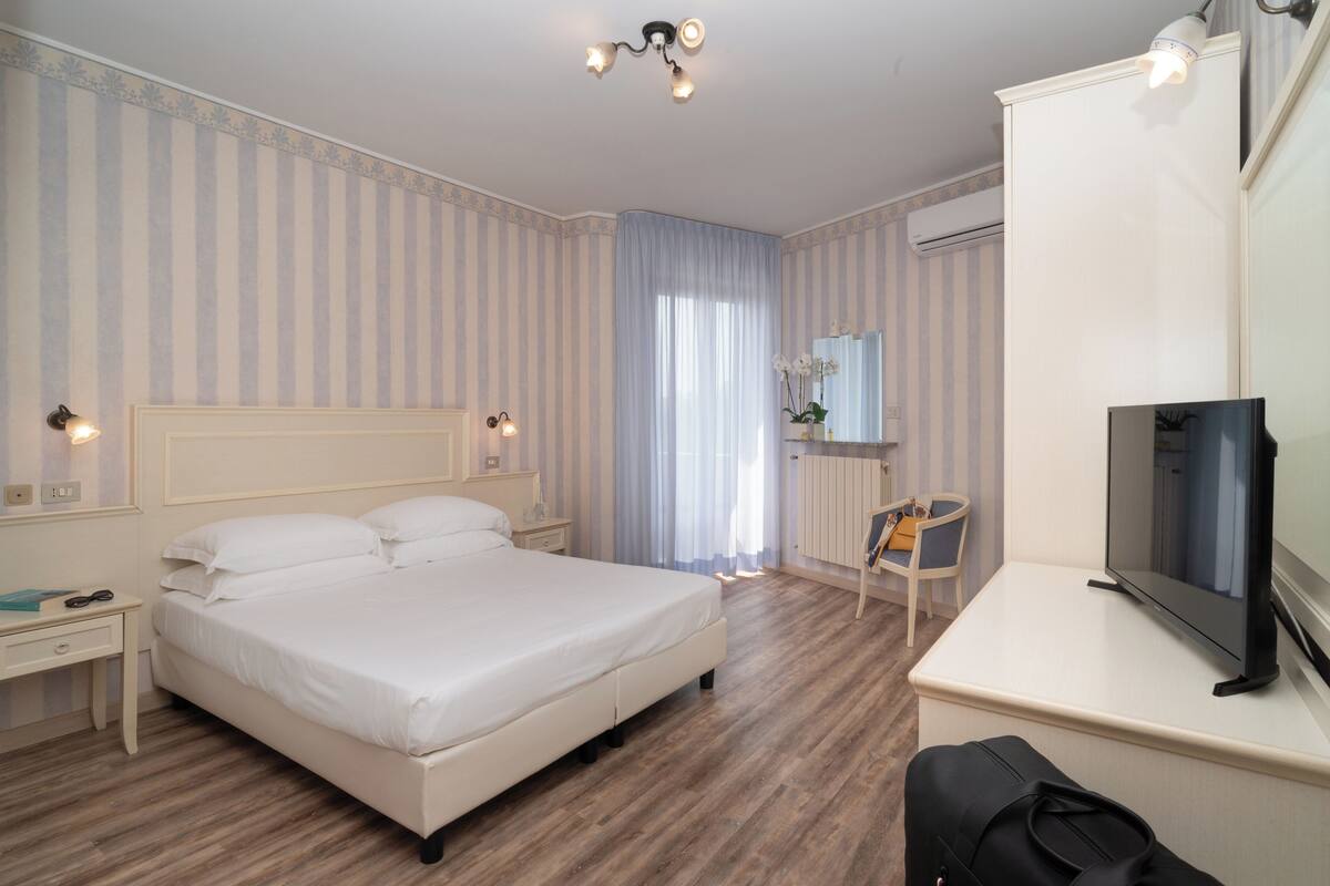 A hotel room with a large bed, a desk with a television, and a chair.
