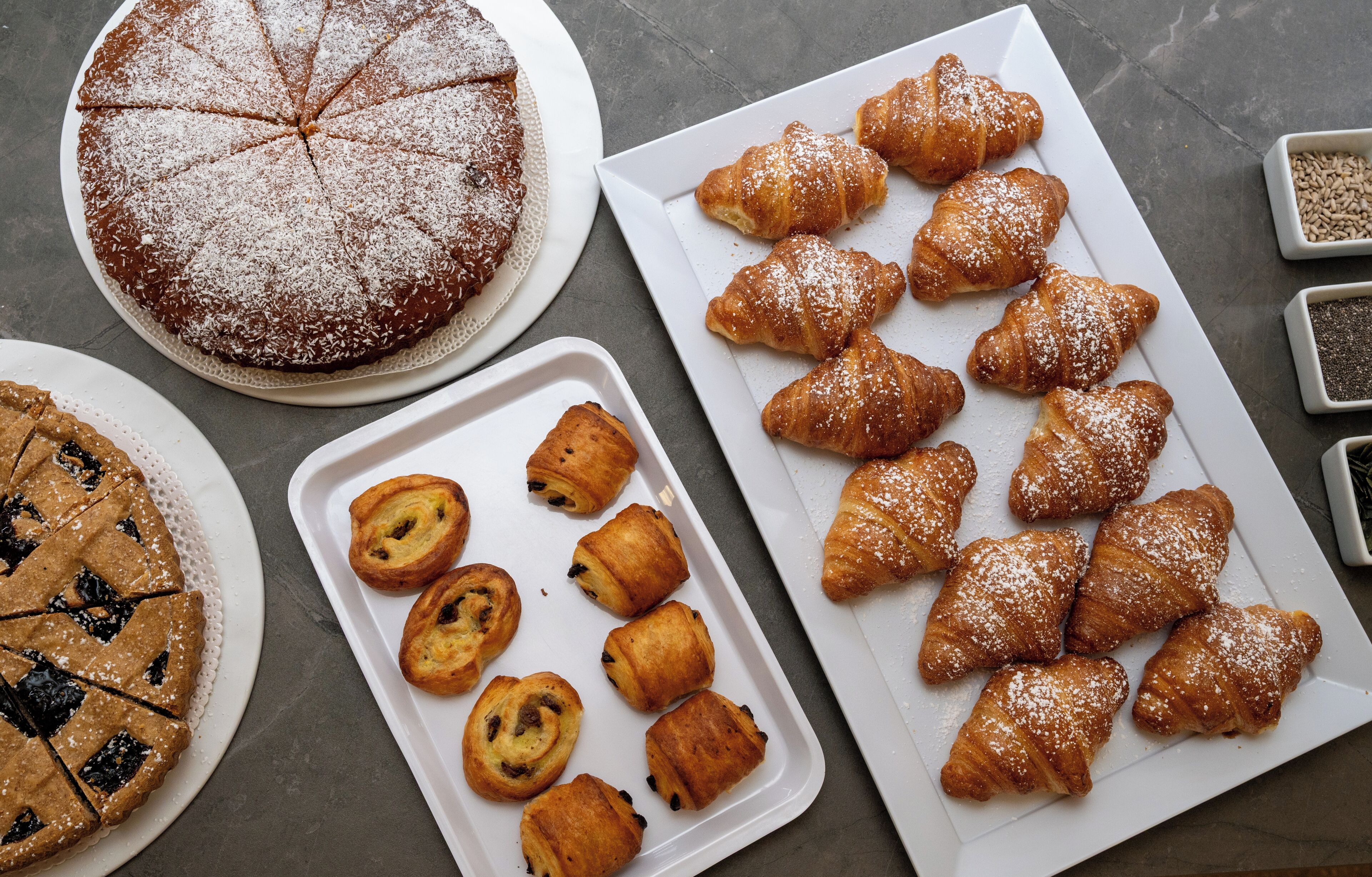 A variety of baked goods including a pie, croissants, and muffins on trays and plates.