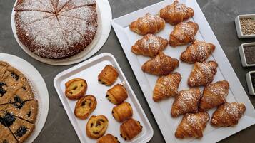 A variety of baked goods including a pie, croissants, and muffins on trays and plates.