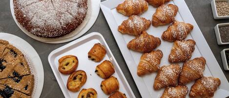 A variety of baked goods including a pie, croissants, and muffins on trays and plates.