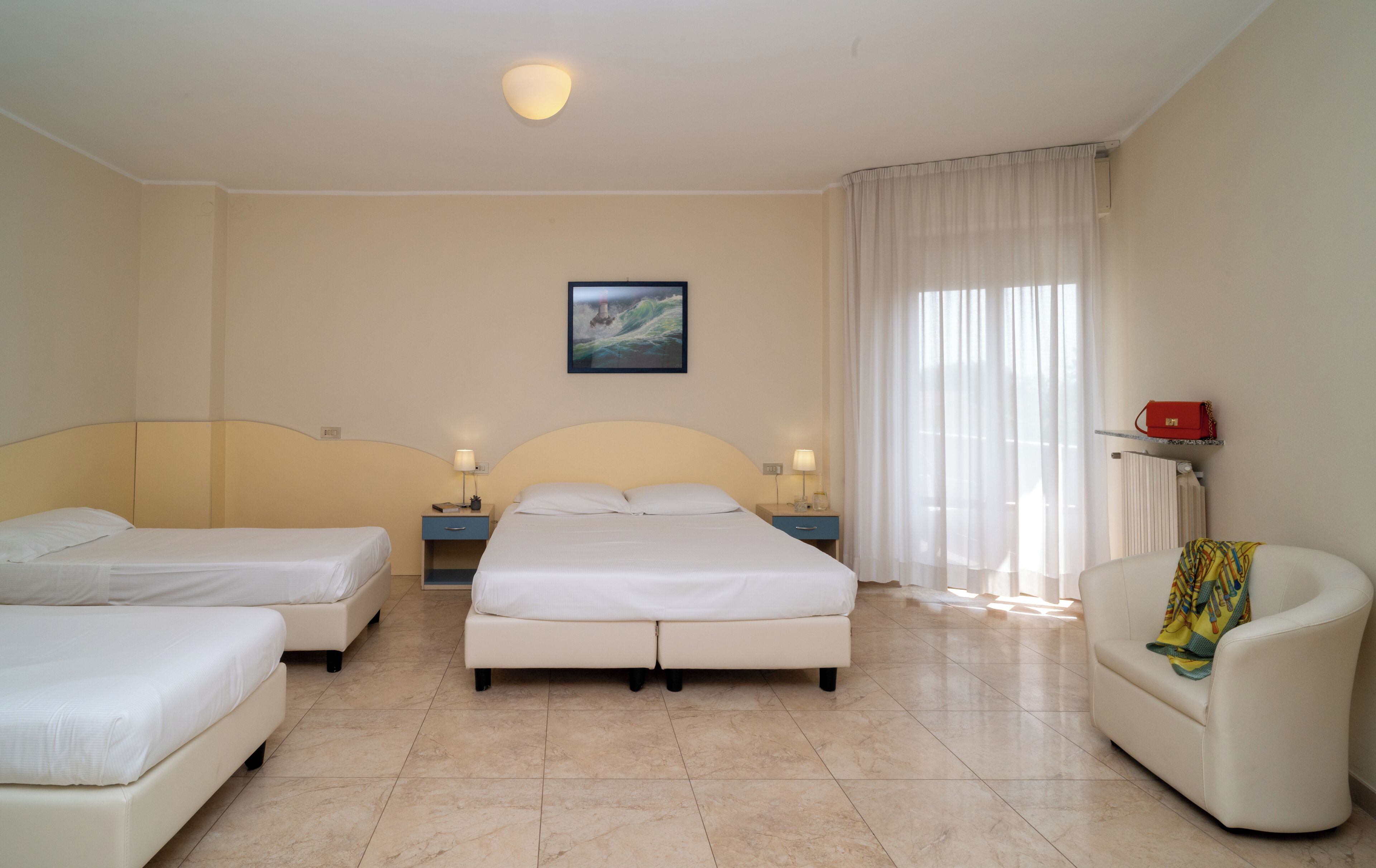 Une chambre d’hôtel avec deux lits simples, un lit double, une chaise, un tableau au mur et une fenêtre avec des rideaux.