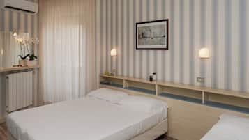 A hotel room with a bed, bedside tables, a mirror, an air conditioner, and a painting on the wall.