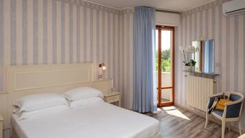 A hotel room with a large bed, a nightstand, a chair, a window with curtains, and a radiator.