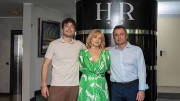 Tres personas de pie frente a un pilar cilíndrico con las letras "HR" y estrellas.