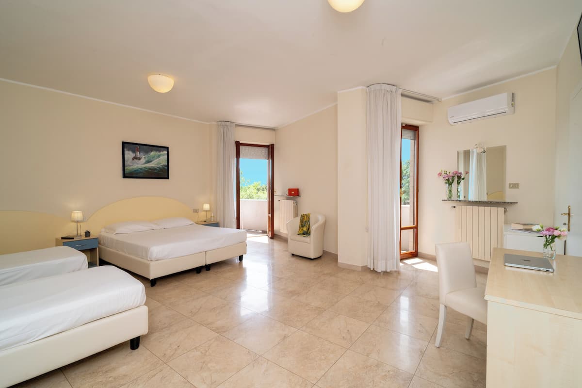 A hotel room with two beds, a desk, a chair, a small table, a lamp, a painting, and an air conditioning unit.