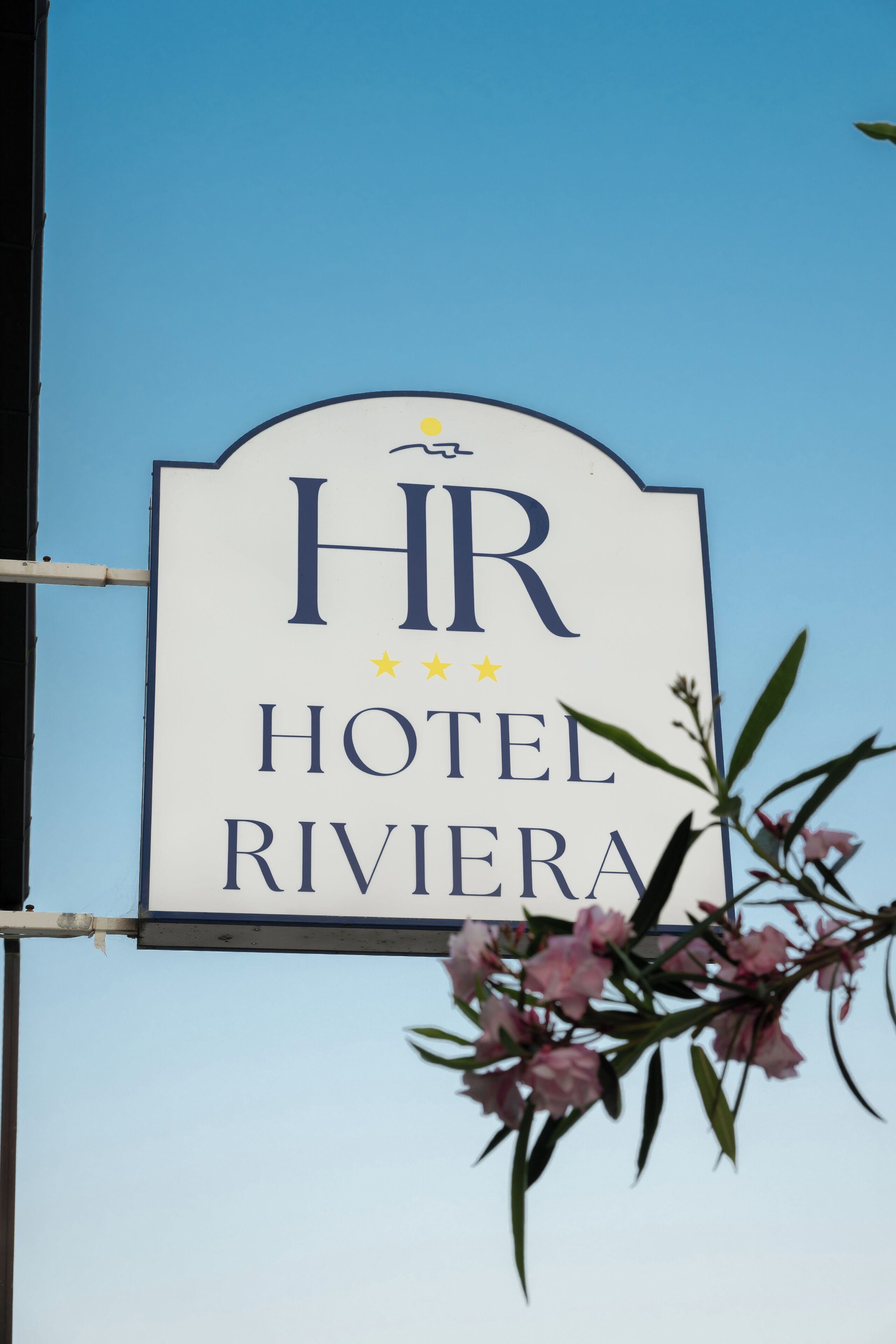 A sign for HR Hotel Riviera with a clear sky in the background.