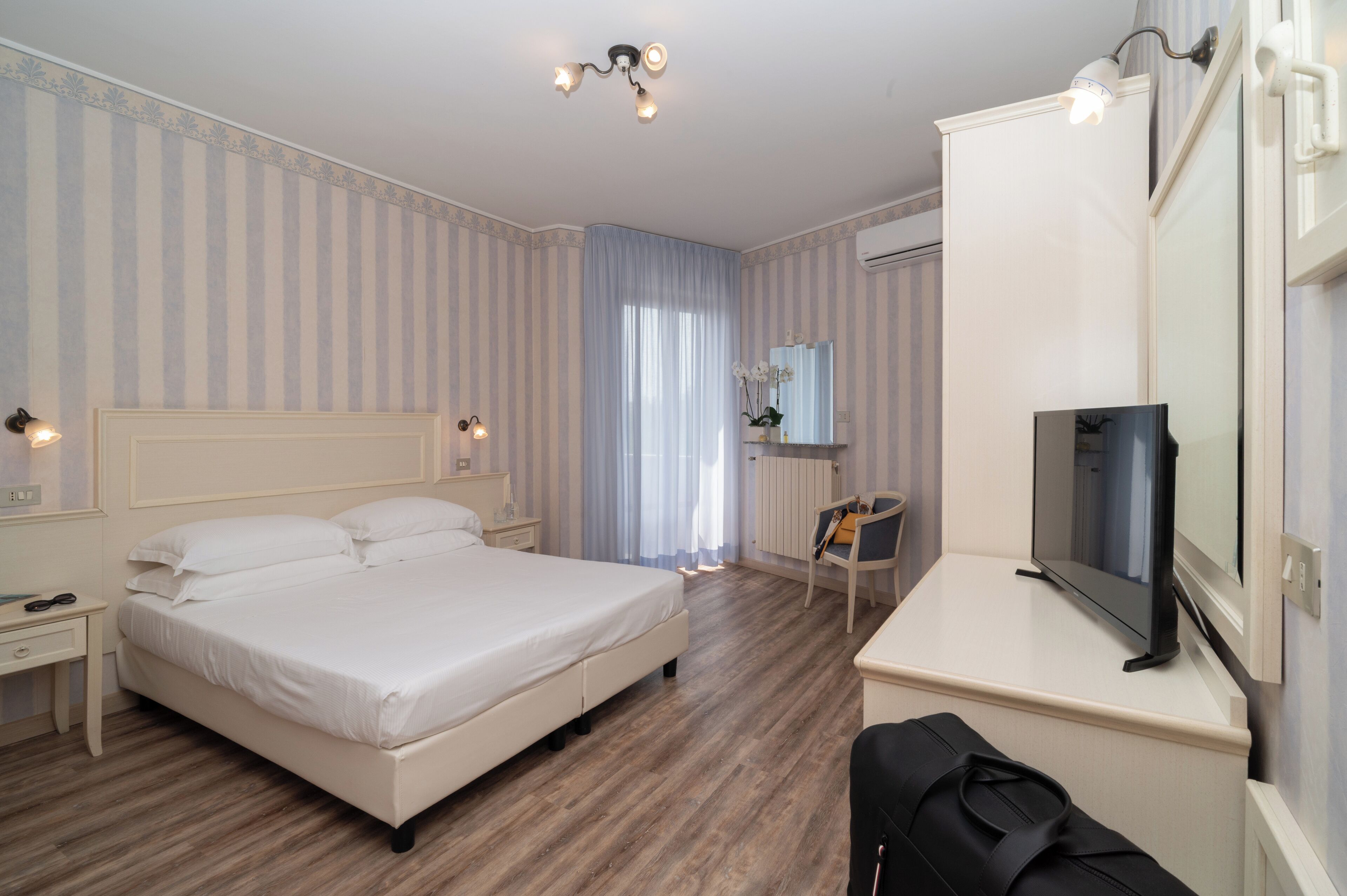 A hotel room with a large bed, a desk with a TV, a chair, and a window with curtains.