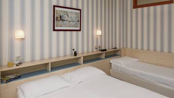 A hotel room with two single beds, a bedside table with a lamp, a framed painting on the wall, and a wooden shelf with a remote control.