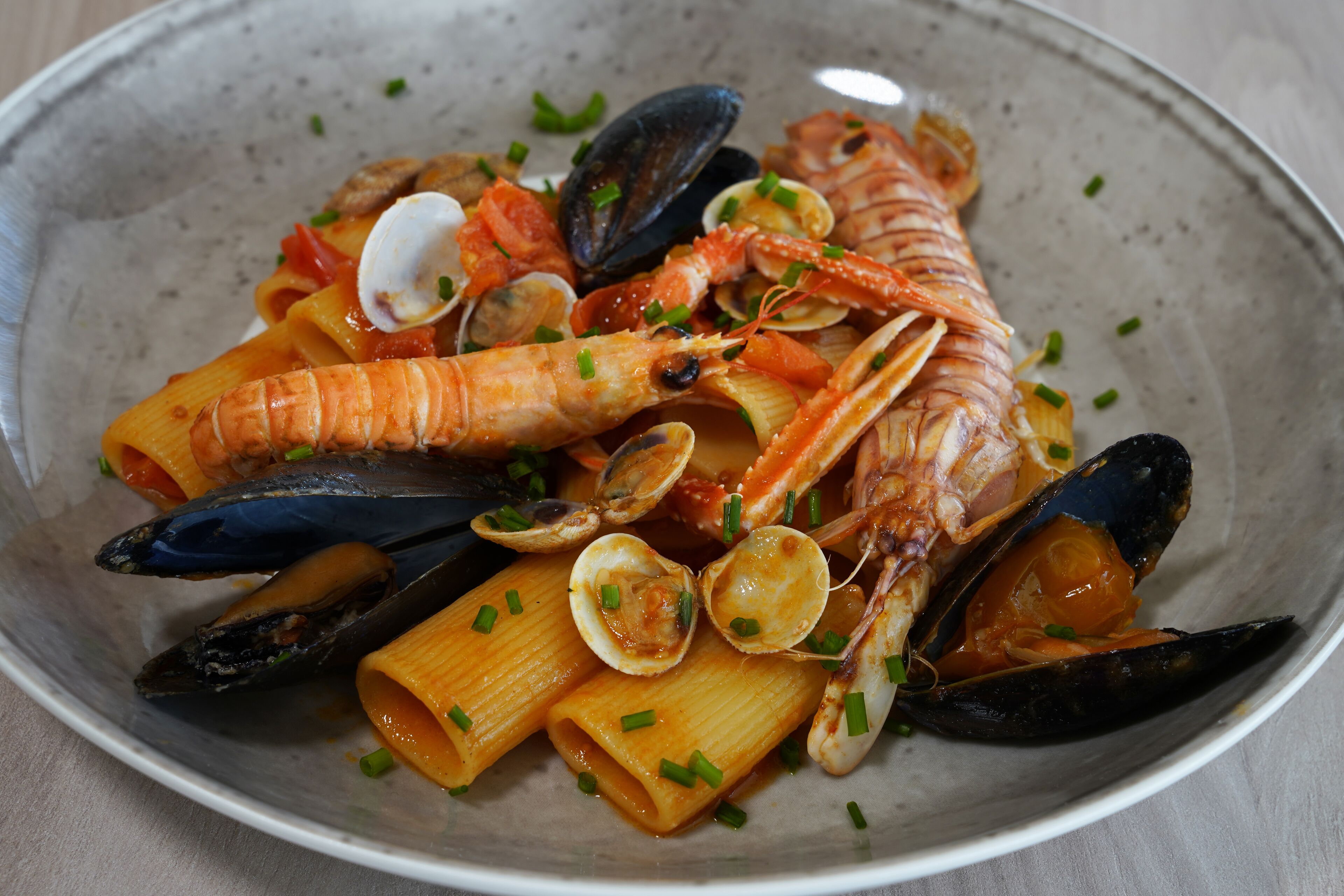 Ein Pasta-Gericht mit Meeresfrüchten, darunter Muscheln, Garnelen und Venusmuscheln, auf einem Teller.