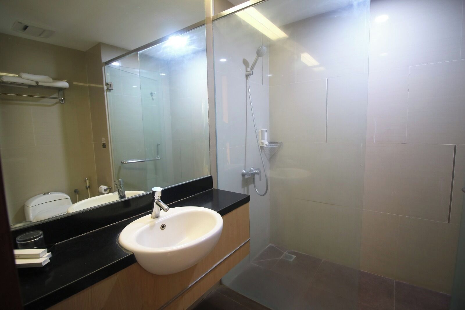 Un baño con lavamanos blanco, un espejo, ducha y perchero para toallas.