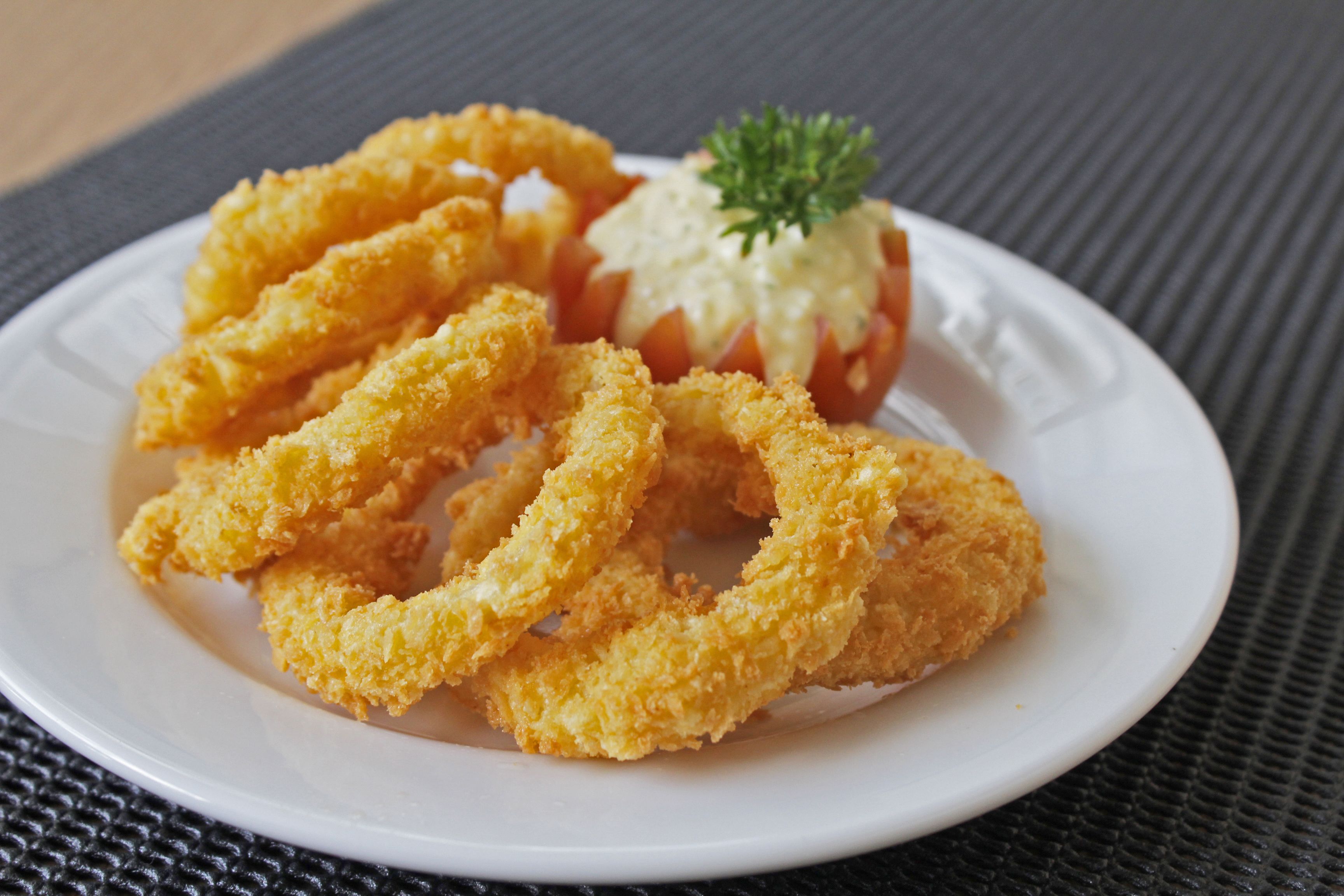 Une assiette de calamars frits accompagnée d’une salade de tomates et d’une garniture.