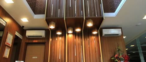 A reception desk with a wooden finish, air conditioning units, and a decorative floral arrangement.